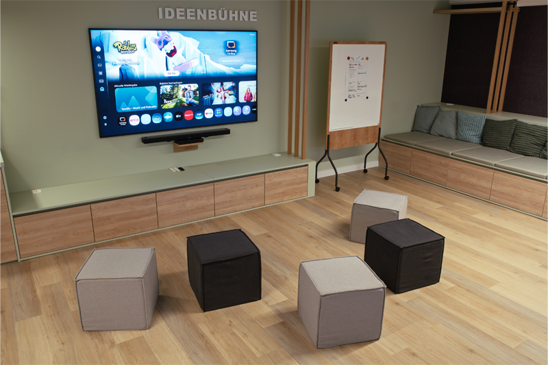 LMZ Ideenbühne Atelier Türke Ideenbühne mit großem Screen, flexiblen Sitzwürfeln und Whiteboard für kollaboratives Arbeiten. Inspirierendes Raumkonzept und mediale Ausstattung von Atelier Türke gestaltet.