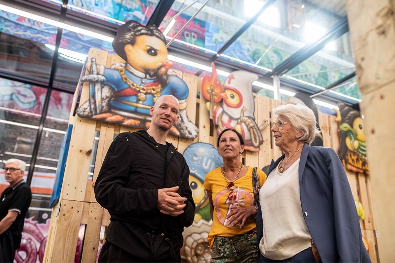 Revolte Impressionen Besucher Kunstwerke Kreativraum Schwelhalle Atelier Türke Besucher im Austausch vor farbenfrohen Urban-Art-Werken erleben die lebendige Atmosphäre der Ausstellung und die kreative Raumgestaltung des Projekts Revolte von Atelier Türke.